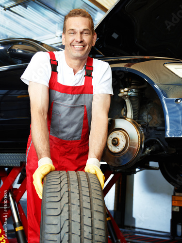 Photo: Smiling motor mechanic in a garage is fitting winter tires Smiling motor mechanic in a garage is fitting winter tires