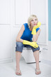 Woman with rubber gloves sitting on the toilet bowl, day dreaming