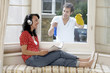 Man cleaning the window while woman is listening to music on headphones and reading a magazine