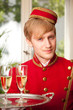 hotelpage in roter uniform serviert chamapgner