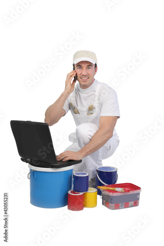 Photo: Decorator with laptop and tins of paint Decorator with laptop and tins of paint