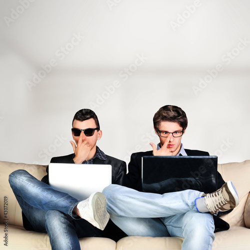 Photo: Two young gamers sitting together on sofa and using their laptop Two young gamers sitting together on sofa and using their laptop