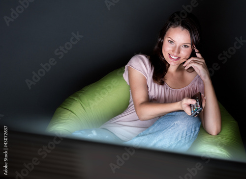 Foto: Young woman watching TV sitting on the beanbag at home Young woman watching TV sitting on the beanbag at home