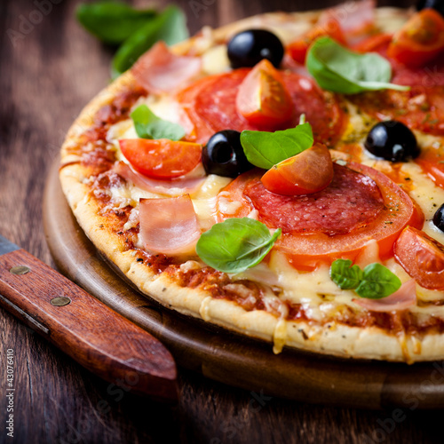 Photo: Pizza with salami, tomatoes and ham on wooden board Pizza with salami, tomatoes and ham on wooden board