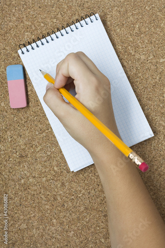 Photo: Pencil with eraser and notebook on cork. Hand Pencil with eraser and notebook on cork. Hand