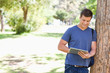 Photo: Student leaning against a tree while using a touch pad Student leaning against a tree while using a touch pad