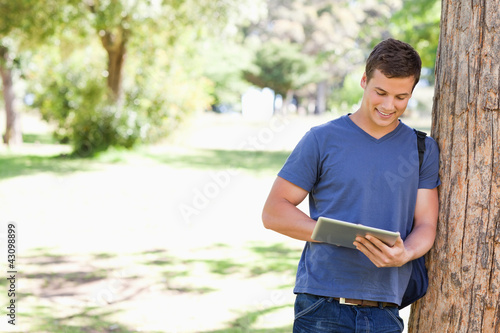 Foto: Student leaning against a tree while using a touch pad Student leaning against a tree while using a touch pad