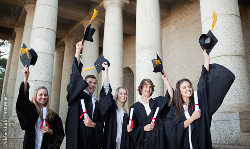 Foto: Smiling graduates holding up their hats Smiling graduates holding up their hats