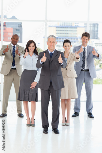 Photo: Business team standing together with their thumbs up in success Business team standing together with their thumbs up in success