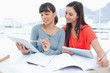 Two smiling students using tablets with one girl looking at the