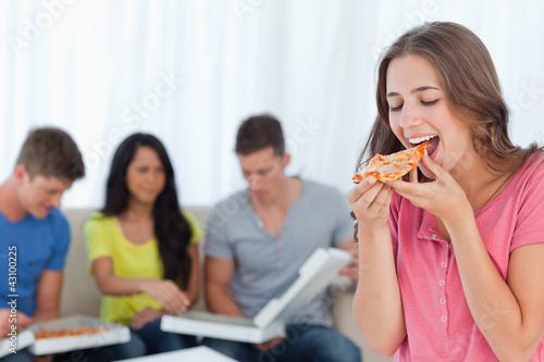 Photo: A woman about to eat a slice of pizza with her friends behind he A woman about to eat a slice of pizza with her friends behind he