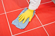 Photo: Worker with yellow gloves and blue towel clean red tiles grout Worker with yellow gloves and blue towel clean red tiles grout