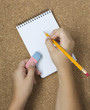 Photo: Pencil with eraser and notebook on cork. Two hands Pencil with eraser and notebook on cork. Two hands