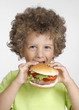 Niño comiendo hamburguesa,sujetando una hamburguesa.