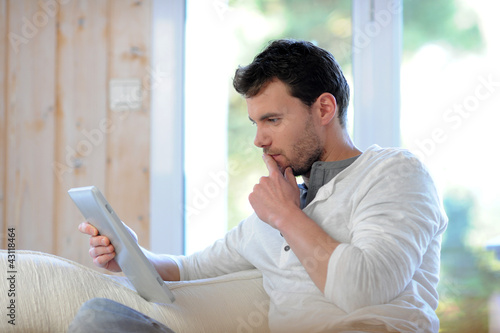 Photo: Handsome man relaxing at home with digital tablet Handsome man relaxing at home with digital tablet