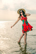 girl in a summer dress and straw hat dancing on the beach