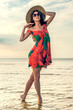 girl in a summer dress and straw hat dancing on the beach