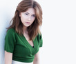 Attractive young woman in green blouse leaning on white wall