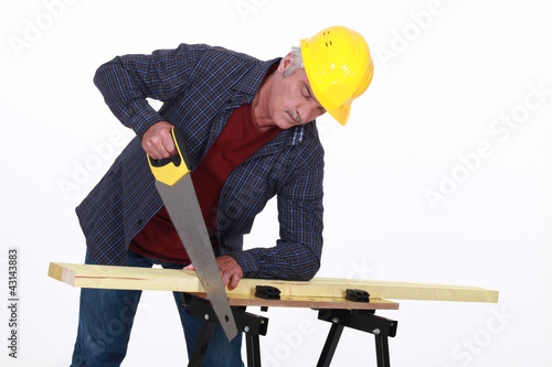 Photo: A mature carpenter sawing. A mature carpenter sawing.