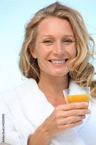 Foto: A woman wearing a dressing gown and drinking orange juice. A woman wearing a dressing gown and drinking orange juice.