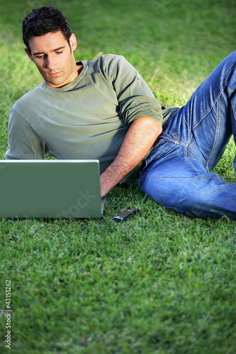 Photo: Man lying on the grass in front of laptop Man lying on the grass in front of laptop