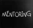 The word "Mentoring" handwritten with white chalk on a blackboar
