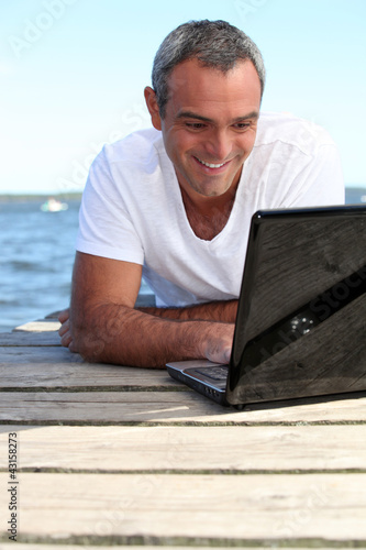 Photo: Man using his laptop on jetty Man using his laptop on jetty
