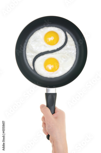 Photo: Fried eggs in the form of yin and yang on pan. Pan in hand on wh Fried eggs in the form of yin and yang on pan. Pan in hand on wh