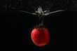 Red apple falling into the water with splash on dark background