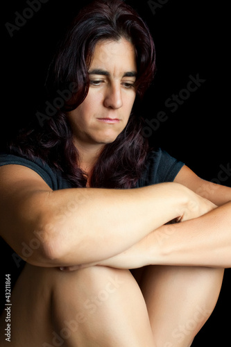 Photo: Sad and worried hispanic woman sitting isolated on black Sad and worried hispanic woman sitting isolated on black