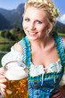 junge blonde Frau im Dirndl mit Masskrug vor Alpenhintergrund