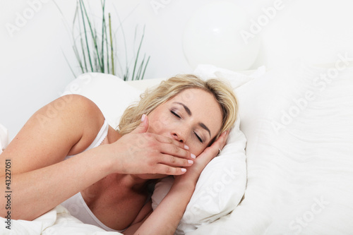 Photo: Young woman lying in her comfortable bed yawning Young woman lying in her comfortable bed yawning