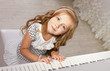 beautiful blond little girl in pretties sitting near a piano