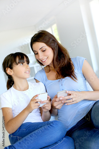 Photo: Mother and daughter using mobile phone at home Mother and daughter using mobile phone at home