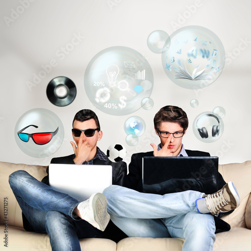 Photo: Two young gamers sitting together on sofa and using their laptop Two young gamers sitting together on sofa and using their laptop