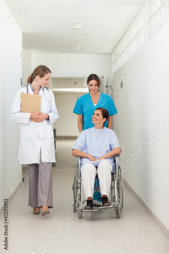 Photo: Nurse pushing a patient in a wheelchair while talking to a docto Nurse pushing a patient in a wheelchair while talking to a docto