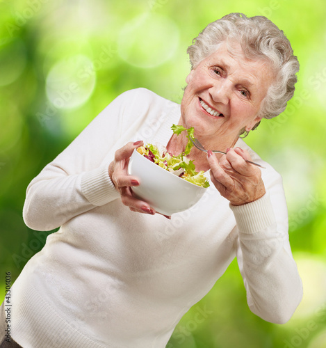 Foto: portrait of senior woman eating a fresh salad against a nature b portrait of senior woman eating a fresh salad against a nature b