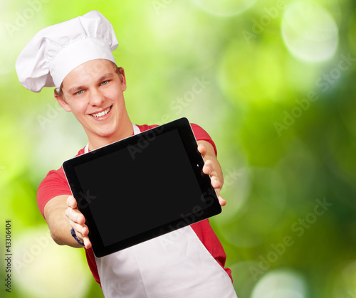 Photo: portrait of young cook man showing a digital tablet against a na portrait of young cook man showing a digital tablet against a na