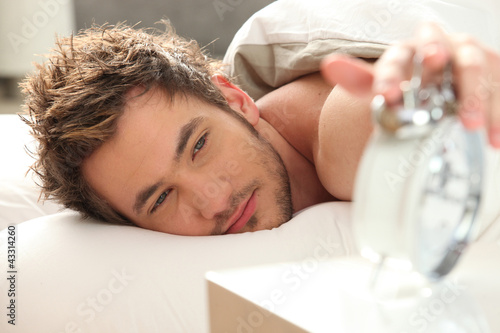 Photo: Man in bed turning off alarm Man in bed turning off alarm