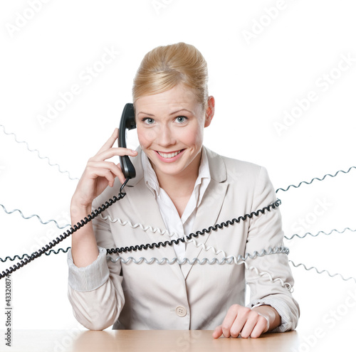 Photo: Young businesswoman sitting at a table tied with phone wire Young businesswoman sitting at a table tied with phone wire