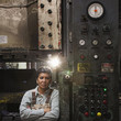 Mixed race worker standing near factory control panel