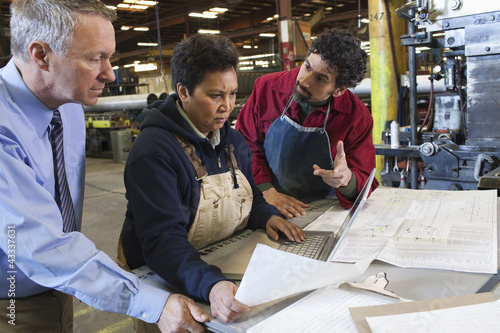 Photo: Foreman and workers looking at paperwork in factory Foreman and workers looking at paperwork in factory