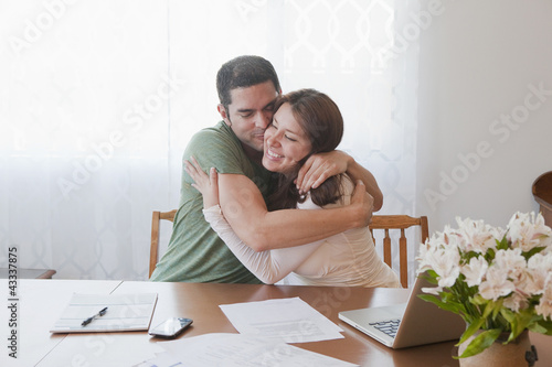 Photo: Hispanic couple paying bills and hugging Hispanic couple paying bills and hugging
