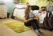 Mixed race teenager sitting on bedroom floor text messaging on cell phone