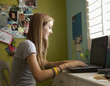 Mixed race teenager using laptop in bedroom