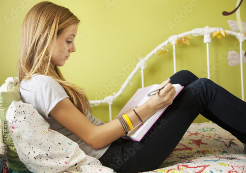 Photo: Mixed race teenager sitting on bed doing homework Mixed race teenager sitting on bed doing homework