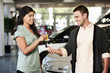 Woman handing man keys to new car in showroom