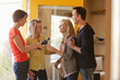 Couple greeting friends arriving with wine