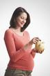 Pregnant Caucasian woman putting money into piggy bank