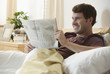 Caucasian man relaxing in bed reading newspaper